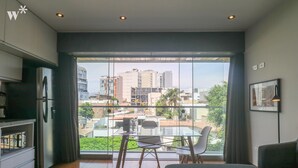 A modern room with a large window, a bed, a dining table with chairs, and a kitchen area. - Wynwood Las Mimosas in Barranco (Lima)