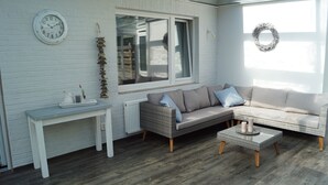 Una habitación acogedora con una pared de ladrillo blanco, un sofá de mimbre, una mesita y un reloj.