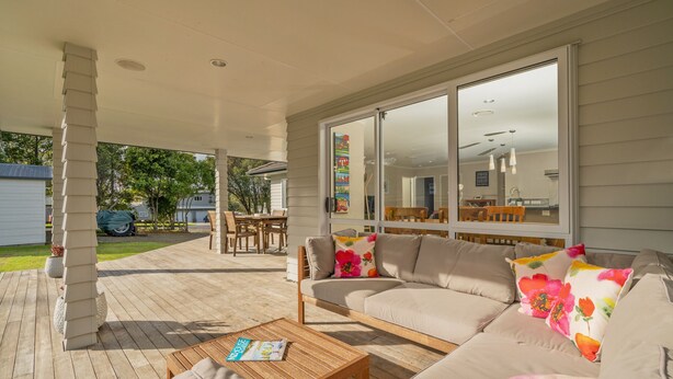 Une terrasse couverte avec un canapé beige, une table basse en bois et un magazine.