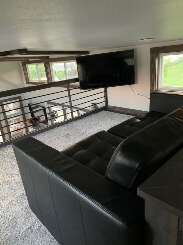 A modern RV interior with a sectional sofa, a mounted TV, and a small dining area.