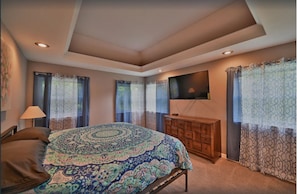 Quarto com cama grande, televisão presa na parede e cômoda de madeira.