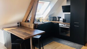 A compact kitchen with a wooden table, black bar stools, and a black cabinet.