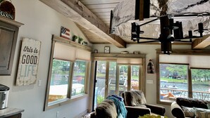 A cozy living room with a wooden ceiling, large windows overlooking a water body, and a comfortable seating area. - New waterfront house with deck,  dock, close to Old Forge, fireplace, , patio (Old Forge)