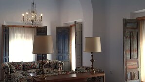 Een woonkamer met een bloemenbank, twee lampen, een kroonluchter en een houten tafel.