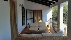Een balkon met een rieten bank, een wijnfles en een glas.
