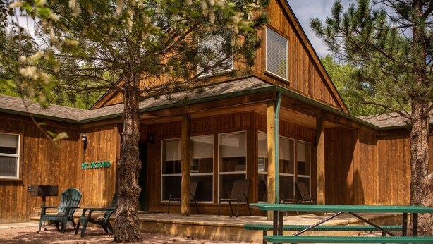 Un bâtiment rustique en bois, doté de grandes fenêtres et d’un espace extérieur aménagé avec des sièges sous une véranda.