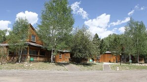 Une rangée de chalets en rondins, dotés de terrasses en bois et de grandes fenêtres, entourés d’arbres.
