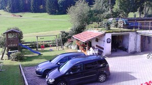 A parking area with two cars, a playground with a slide, and a building with a red roof. - Ihr Ferienhof am Rande der Alpen, Nebenhaus (Seeg)