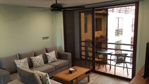 Un salon comprenant un canapé, une table basse et une porte-fenêtre coulissante donnant sur un balcon aménagé avec du mobilier d’extérieur.