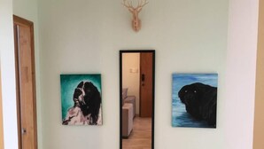 Un couloir avec trois œuvres d’art encadrées accrochées au mur, une porte en bois sur la gauche et un miroir qui reflète une pièce avec un canapé et une porte.