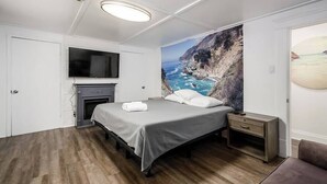 Ein Schlafzimmer mit Bett, Fernseher über einem Kamin und einer großen Küstenmalerei an der Wand.