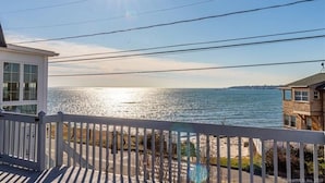 A coastal view from a balcony with a railing, overlooking the sea and a distant shoreline. - Sleep to the sound of the waves. Watch the sun set from the deck! Secluded beach (East Lyme)
