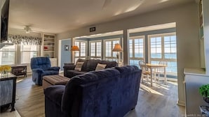 A spacious living room with a large window overlooking the sea, a ceiling fan, and a dining area with a view. - Sleep to the sound of the waves. Watch the sun set from the deck! Secluded beach (East Lyme)