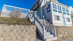 A two-story house with a stone retaining wall and a wooden staircase leading to the entrance. - Sleep to the sound of the waves. Watch the sun set from the deck! Secluded beach (East Lyme)