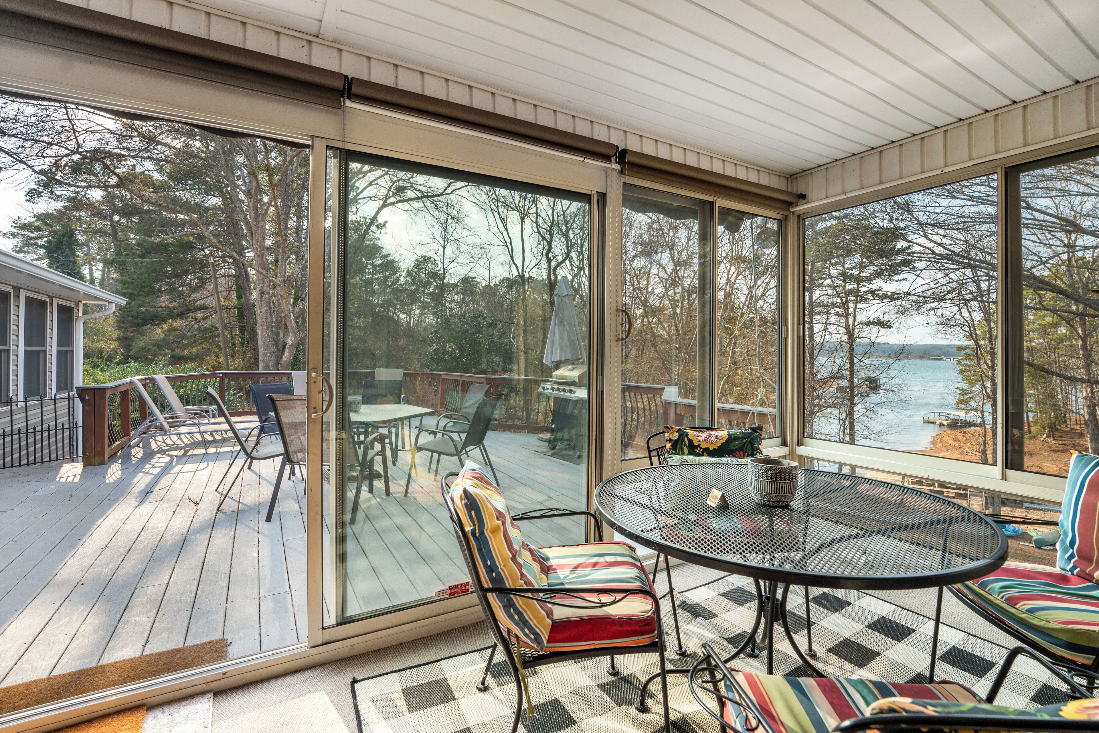A covered deck with a glass door, outdoor furniture, and a view of a lake.