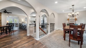 A spacious dining area with a wooden table and chairs, a chandelier, and a staircase leading to an upper level.