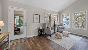 A spacious living room with hardwood flooring, a large window with a view, and a door leading to an outdoor area.