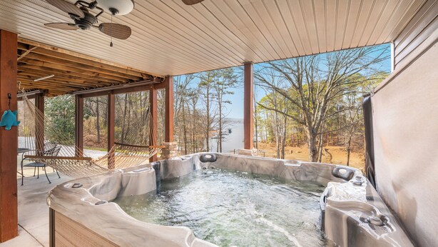 A hot tub with a wooden deck and a hammock, surrounded by trees and a clear sky.