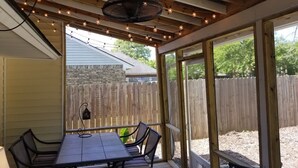 Une terrasse couverte avec une table et des chaises, un ventilateur suspendu et des guirlandes lumineuses.