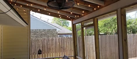 A covered patio with a table and chairs, a hanging fan, and string lights.
