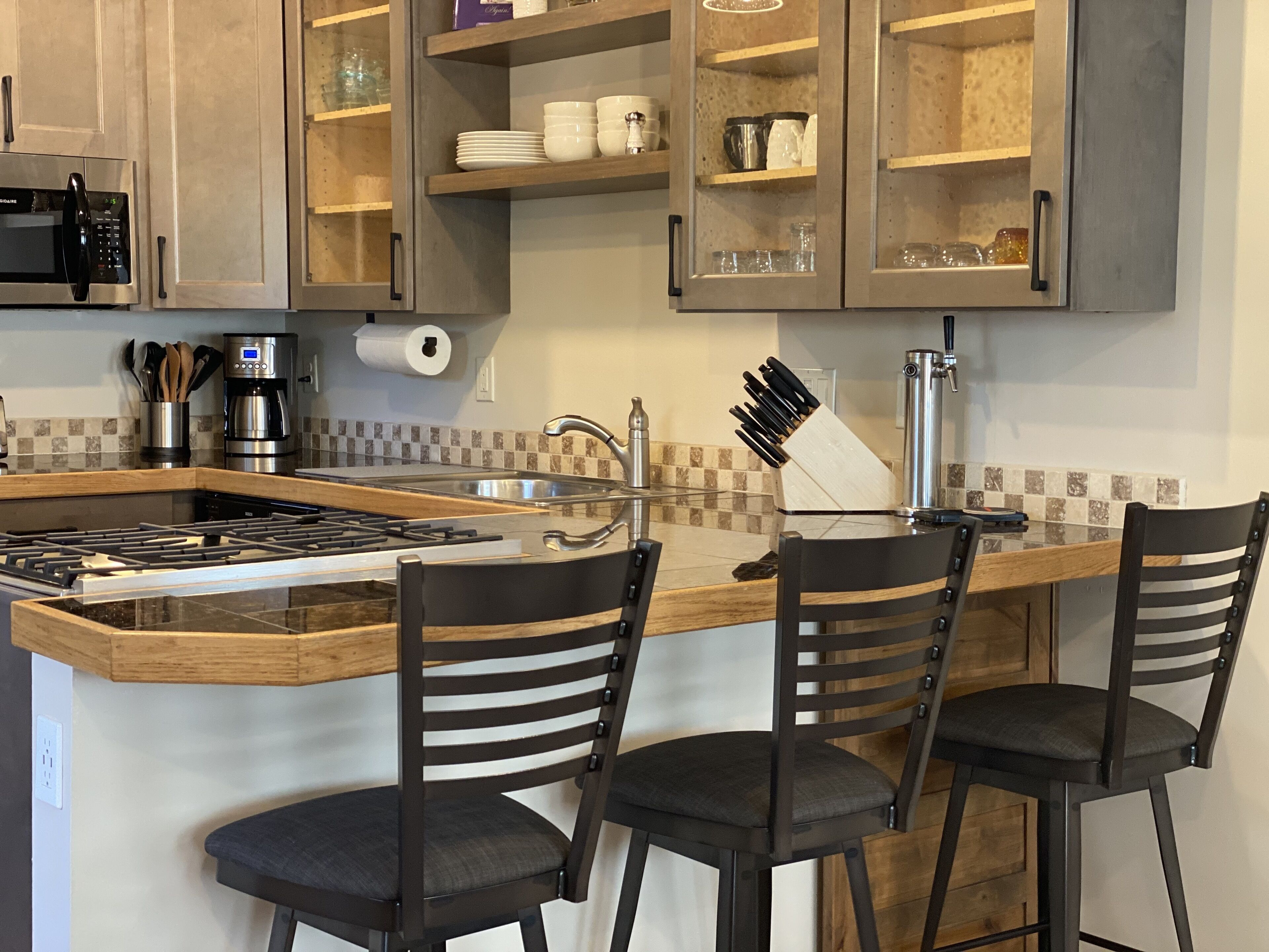 Une cuisine dotée d’un îlot central, de tabourets de bar, d’une cuisinière encastrée et d’une machine à café.