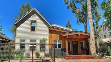 Une maison à deux étages dotée d’un porche en bois et d’un mur de soutènement en pierre.