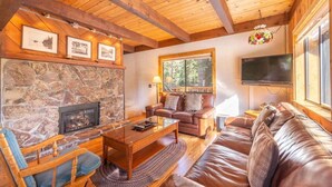 Una sala de estar acogedora con chimenea de piedra, mobiliario de cuero, vigas de madera y un ventanal grande.