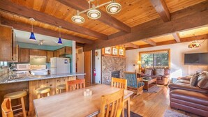 Interior rústico de una cabaña con una mesa de comedor de madera, zona de bar y una sala de estar acogedora con chimenea.