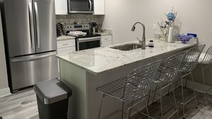 A modern kitchen with stainless steel appliances, a marble countertop, and a bar area with metal chairs.