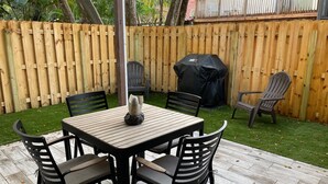 A patio with a wooden table and chairs, a barbecue grill, and a wooden fence.