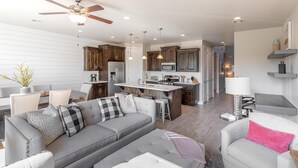 Una sala de estar moderna con un sofá y un sillón, ambos grises, y un comedor con una cocina al fondo.