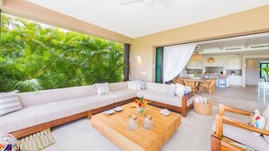 Una sala de estar moderna con un sofá grande, una mesa de centro de madera y vistas a abundante vegetación.
