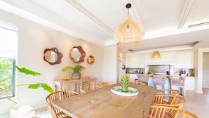Un comedor espacioso con una mesa de madera y sillas de mimbre, una cocina al fondo y espejos decorativos en las paredes.