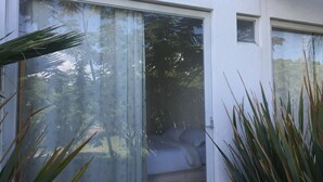 A modern room with a large sliding glass door leading to a balcony, a bed with white bedding, and a view of trees and greenery outside. - Nice Cozy Apartment in Juriquilla (Qro.)