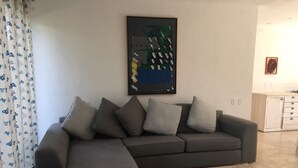 A modern living room with a grey sectional sofa, a coffee table, and a painting on the wall. - Nice Cozy Apartment in Juriquilla (Qro.)