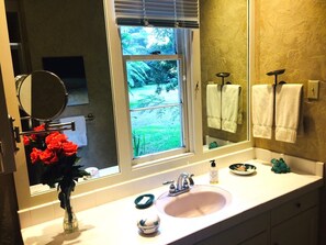 Ein Badezimmer mit einem großen Fenster, einem Waschbecken, einem Spiegel und einer Blumenvase.