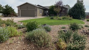 A residential house with a garage, a well-maintained lawn, and various shrubs and plants. - Spacious and Comfortable Garden Level Basement Apartment (Peyton)