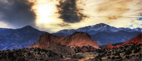 A mountainous landscape with a prominent rock formation in the foreground and snow-capped mountains in the background.