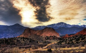 A mountainous landscape with a prominent rock formation in the foreground and snow-capped mountains in the background.