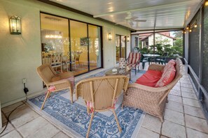Relax in this open-plan living area with a sofa, chairs, and a patterned rug, featuring a sliding glass door to a balcony with a view of the surrounding greenery.