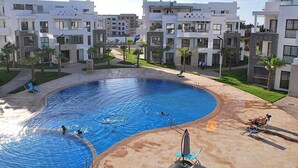 A swimming pool surrounded by modern buildings with balconies, palm trees, and a clear sky. - Residence Hivernage Founty 4773 (Agadir)