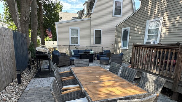 An outdoor patio with a wooden table and wicker chairs, surrounded by a stone pathway and a wooden fence. - Beach Vacation Getaway (Old Orchard Beach)