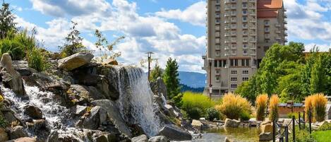 A waterfall, a pond, and a hotel building with multiple floors and balconies.