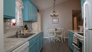Una cocina con armarios verde mar, una encimera blanca, una araña y una mesa de comedor con sillas.