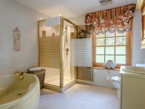 Un baño con ducha de vidrio, bañera, inodoro y ventana con cortina decorativa.