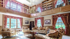 Un salon spacieux et élégamment aménagé, doté d’un haut plafond, de bibliothèques en bois richement décorées et d’un coin salon confortable.
