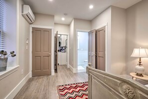 A hallway with beige walls, wooden flooring, and a zigzag patterned rug. There are two doors, a mirror, and a lamp on a side table.
