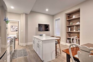 Una cocina moderna con armarios blancos, una isla central y un comedor con mesa y sillas de madera.