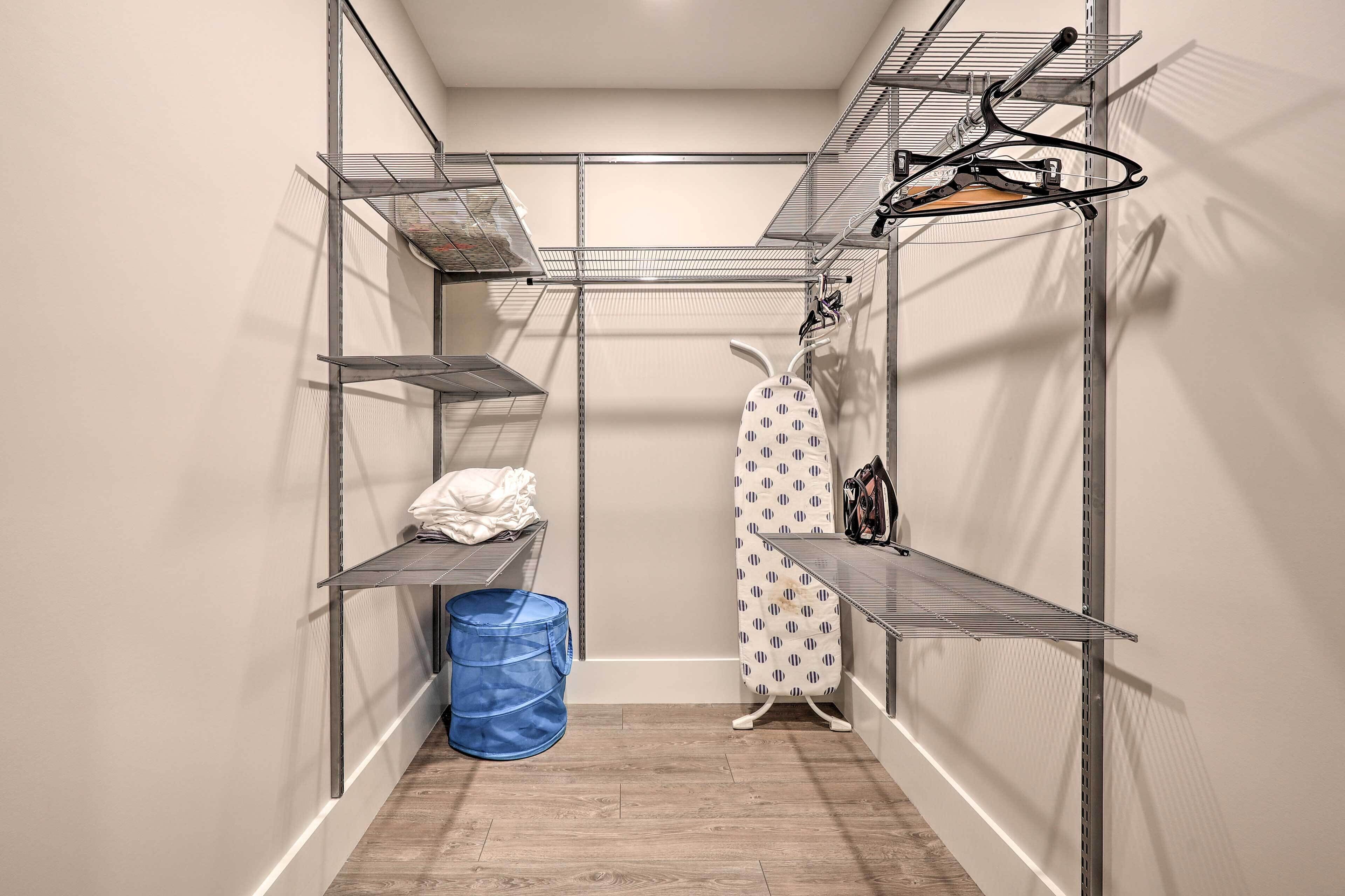 Uma lavanderia compacta com estantes de metal, um espaço para passar roupa e uma lixeira azul.