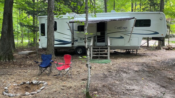 Un camping-car blanc doté d’un porche couvert et d’une échelle menant à l’entrée. Deux chaises sont placées à l’extérieur.